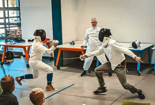 two fencers in a demonstration bout at the LINC with coach bill referring in the background