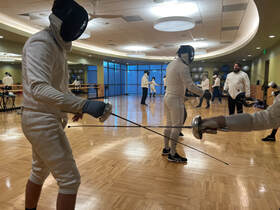 two fencers practicing parries in class with students in background